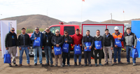 A group of people standing outdoors, holding blue bags labeled 'Teck', in front of a red vehicle.